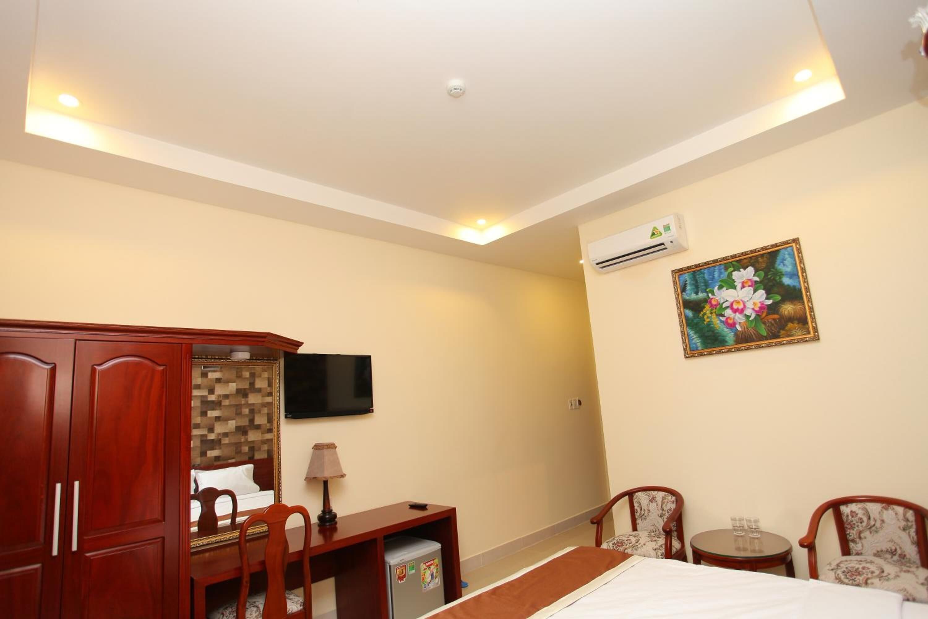 A hotel room with a bed, a desk with a chair, a small table with two chairs, a TV mounted on the wall, and an air conditioning unit.