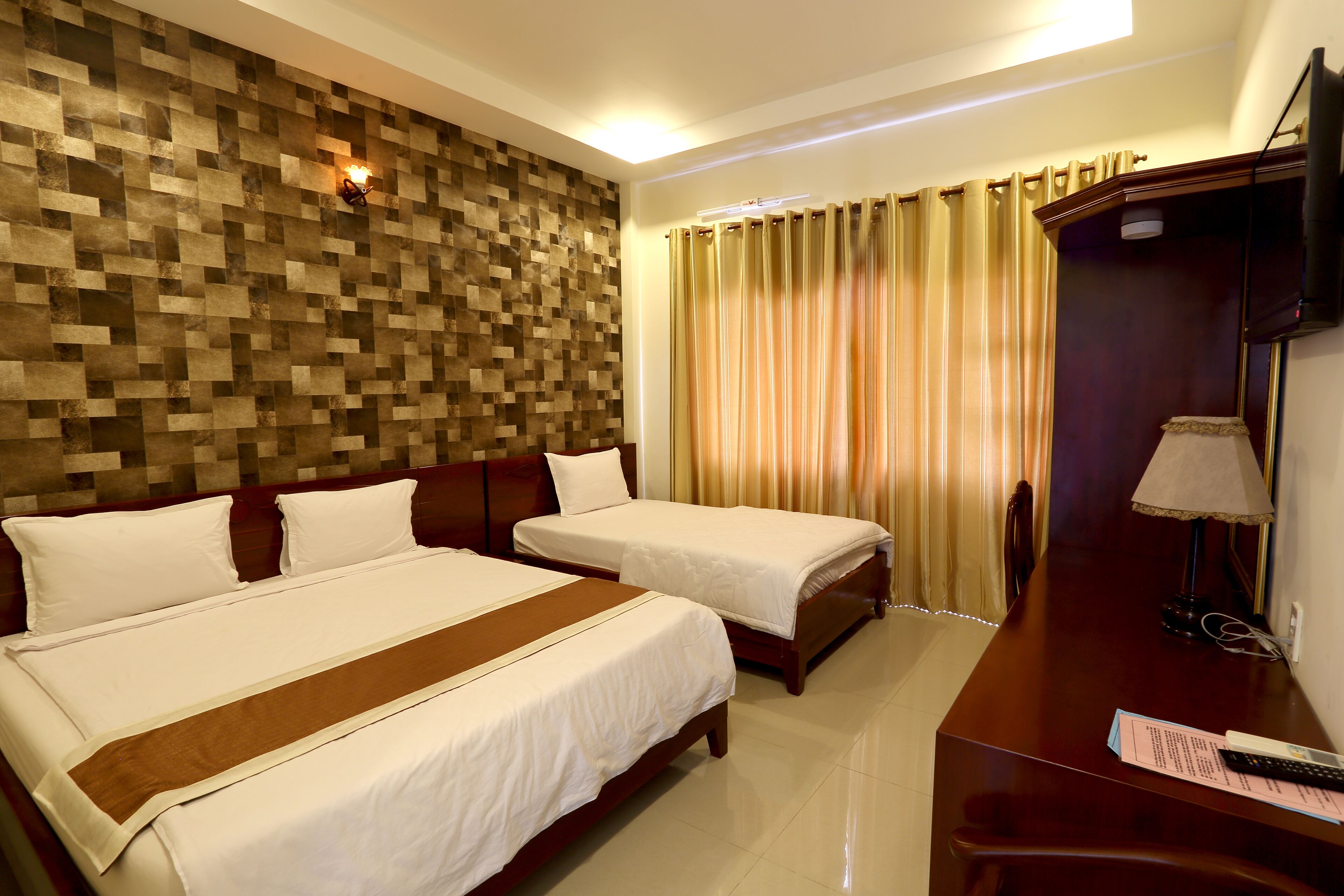 A hotel room with two beds, a wooden wall panel, a desk with a lamp, and a television.