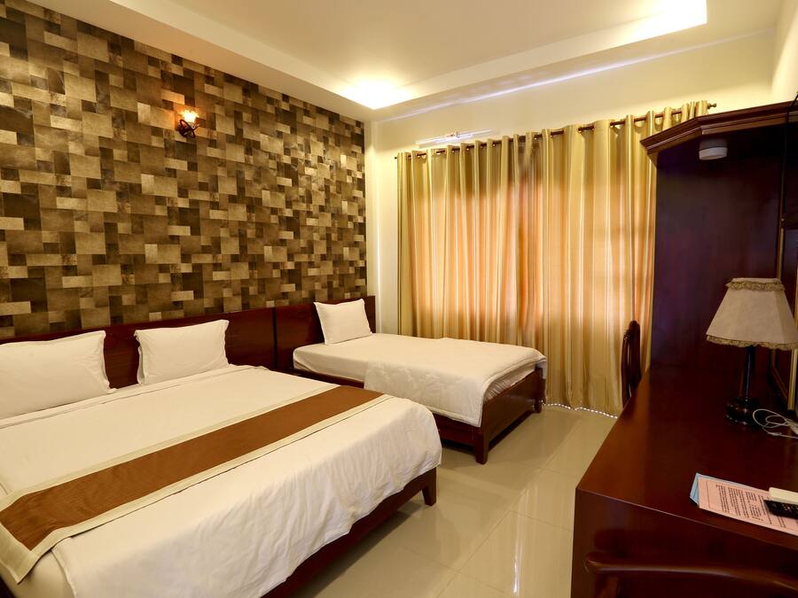 A hotel room with two beds, a wooden wall panel, a desk with a lamp, and a television.