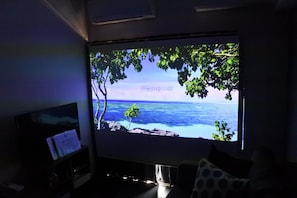 Une pièce dotée d’un grand téléviseur à écran plat qui diffuse une vue panoramique sur une plage et l’océan.