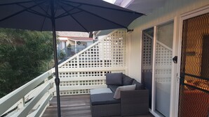 A balcony with a wooden deck, a black umbrella, a sofa with cushions, and a white railing. - Lakeside Beach House - Child & Dog Friendly (Loch Sport)