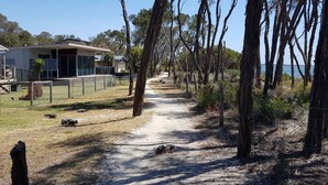 A pathway leading to a building with a fenced area, surrounded by trees and a clear view of the sea. - Lakeside Beach House - Child & Dog Friendly (Loch Sport)