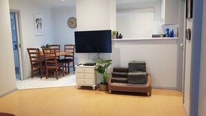 A compact living space with a dining area, a flat-screen TV mounted on the wall, a sofa, a small table, and a potted plant. - Lakeside Beach House - Child & Dog Friendly (Loch Sport)