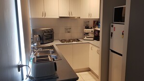 A compact kitchen with white cabinets, a built-in oven, a stove, a toaster, and a refrigerator. - Lakeside Beach House - Child & Dog Friendly (Loch Sport)