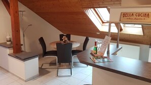 Et spiseområde med træloft, et rundt bord og sorte stole. Et skilt viser 'Bella Cucina Buon Appetito'.