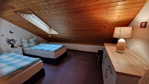 Una camera da letto con due letti, un lucernario, soffitto in legno, un comodino con una lampada e una piccola cassettiera.