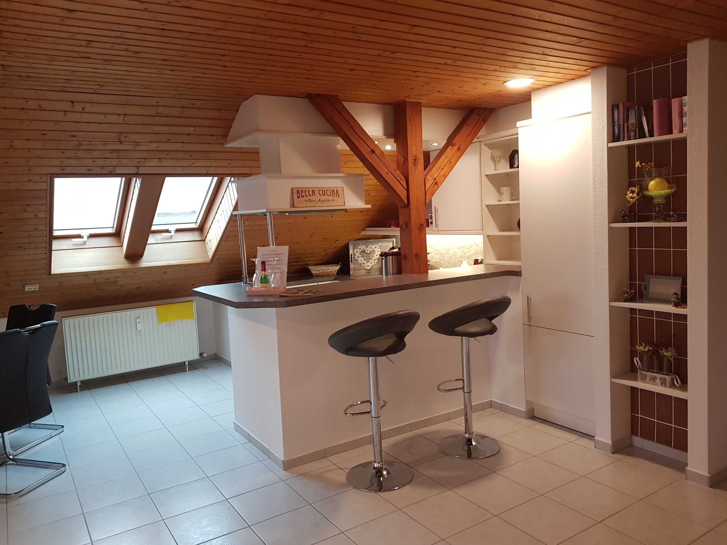 Eine Küche mit Holzbalkendecke, einer Arbeitsplatte mit Barhocker und einem Fenster.