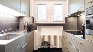 A modern kitchen with grey cabinetry, a black countertop, a built-in oven, and a window above the sink. - Appartements Hofquartier (Lucerne)