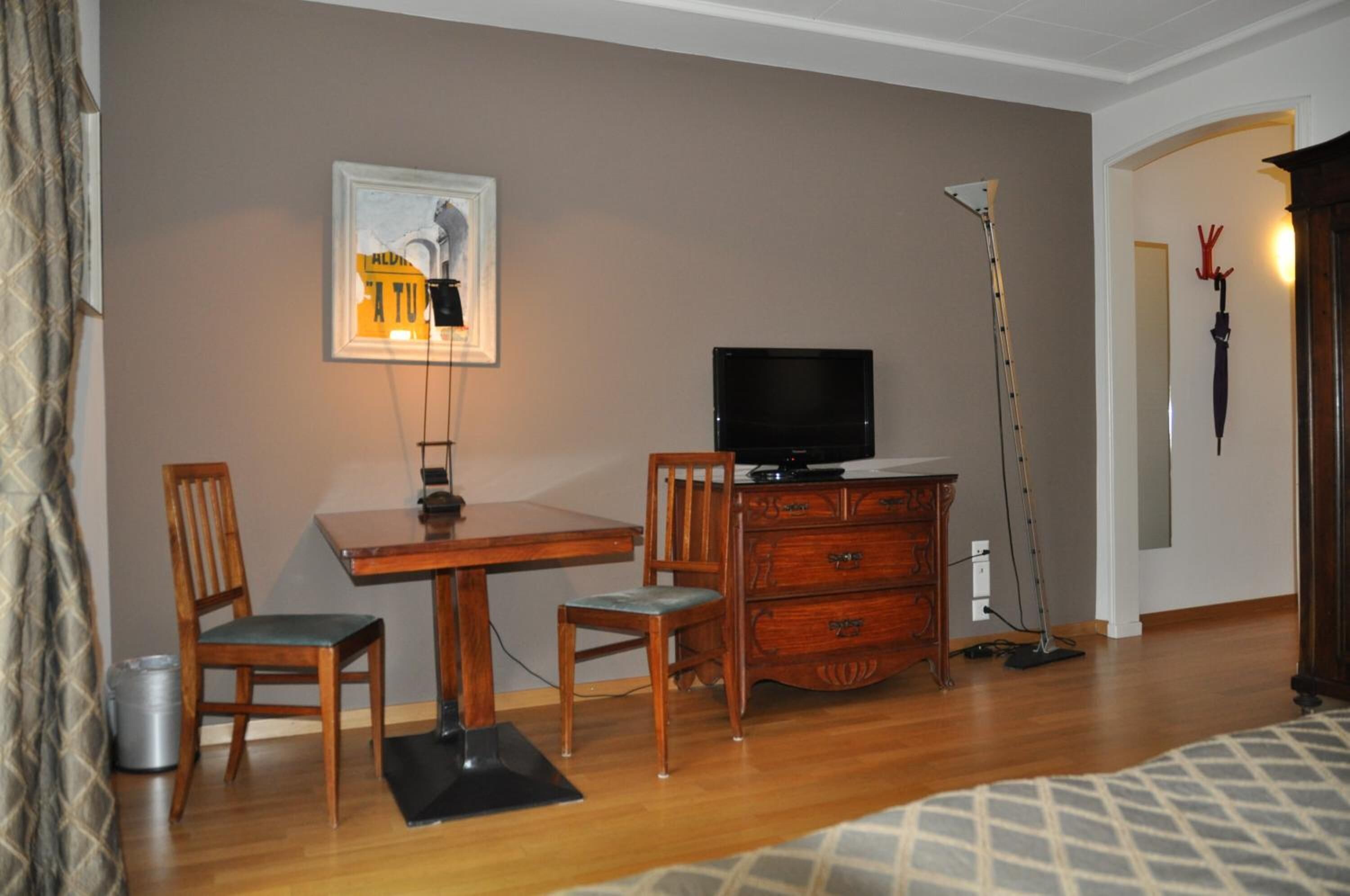 A room with a wooden desk, two chairs, a television, a lamp, and a vacuum cleaner.