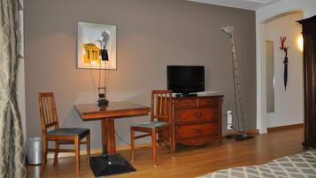 A room with a wooden desk, two chairs, a television, a lamp, and a vacuum cleaner.