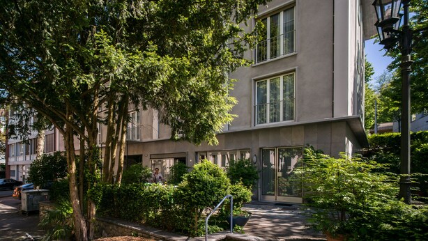 A modern building with a flat facade, large windows, and a well-maintained garden with trees and shrubs. - Appartements Hofquartier (Lucerne)