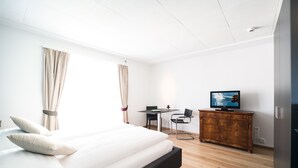 A hotel room with a large bed, a desk, a television, and a wardrobe. - Appartements Hofquartier (Lucerne)