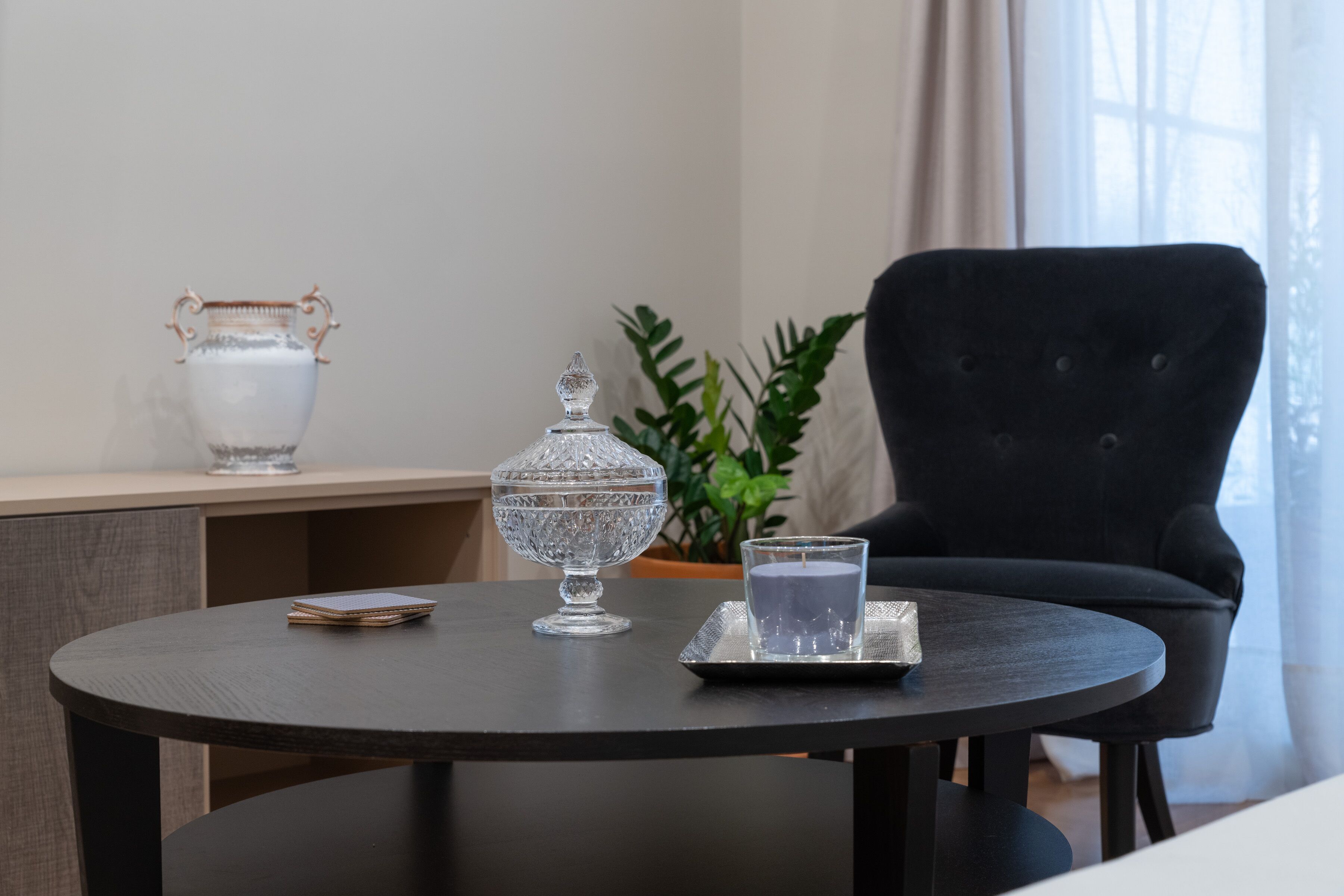 A round table with a dark finish, a white vase, a glass candle holder, and a glass candle on a tray.