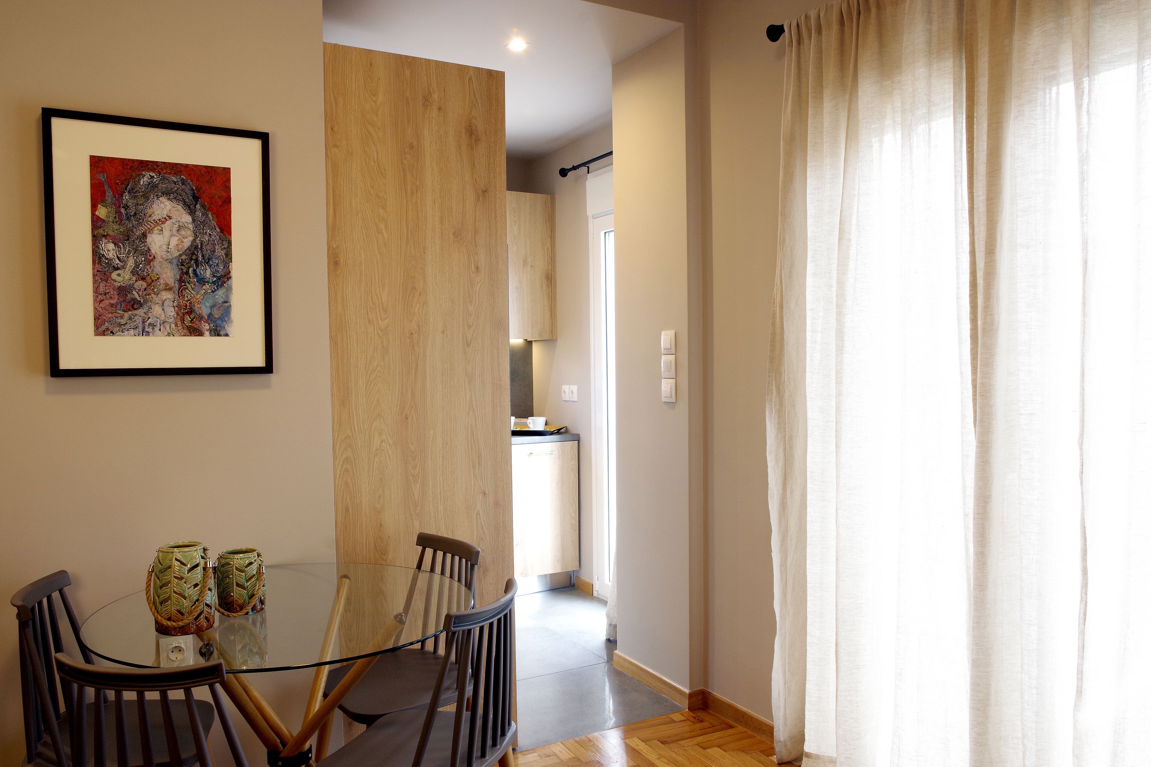 A dining area with a glass table, chairs, and a framed artwork on the wall.