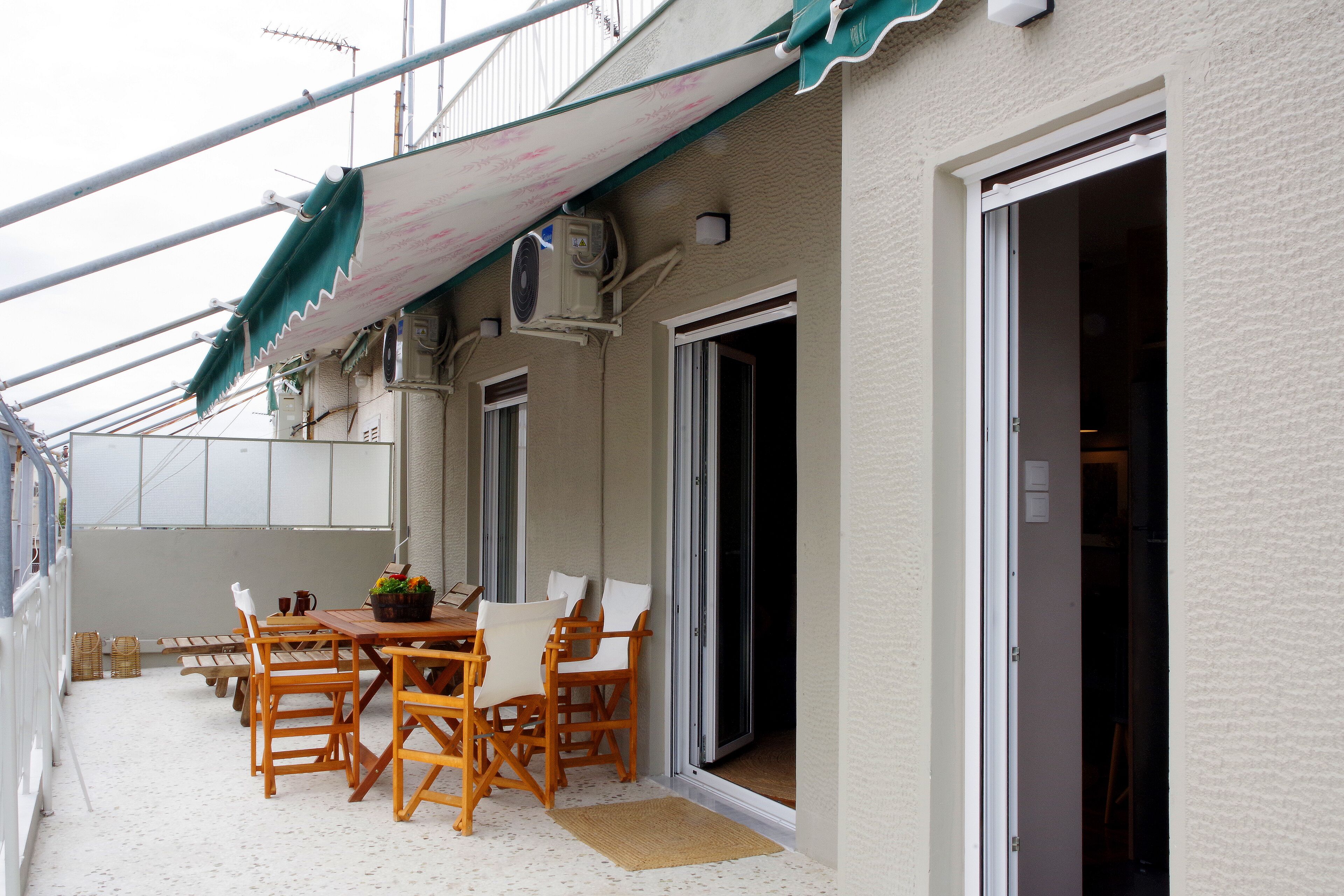 A covered outdoor seating area with a table and chairs, a potted plant, and a sliding glass door leading to an interior space.
