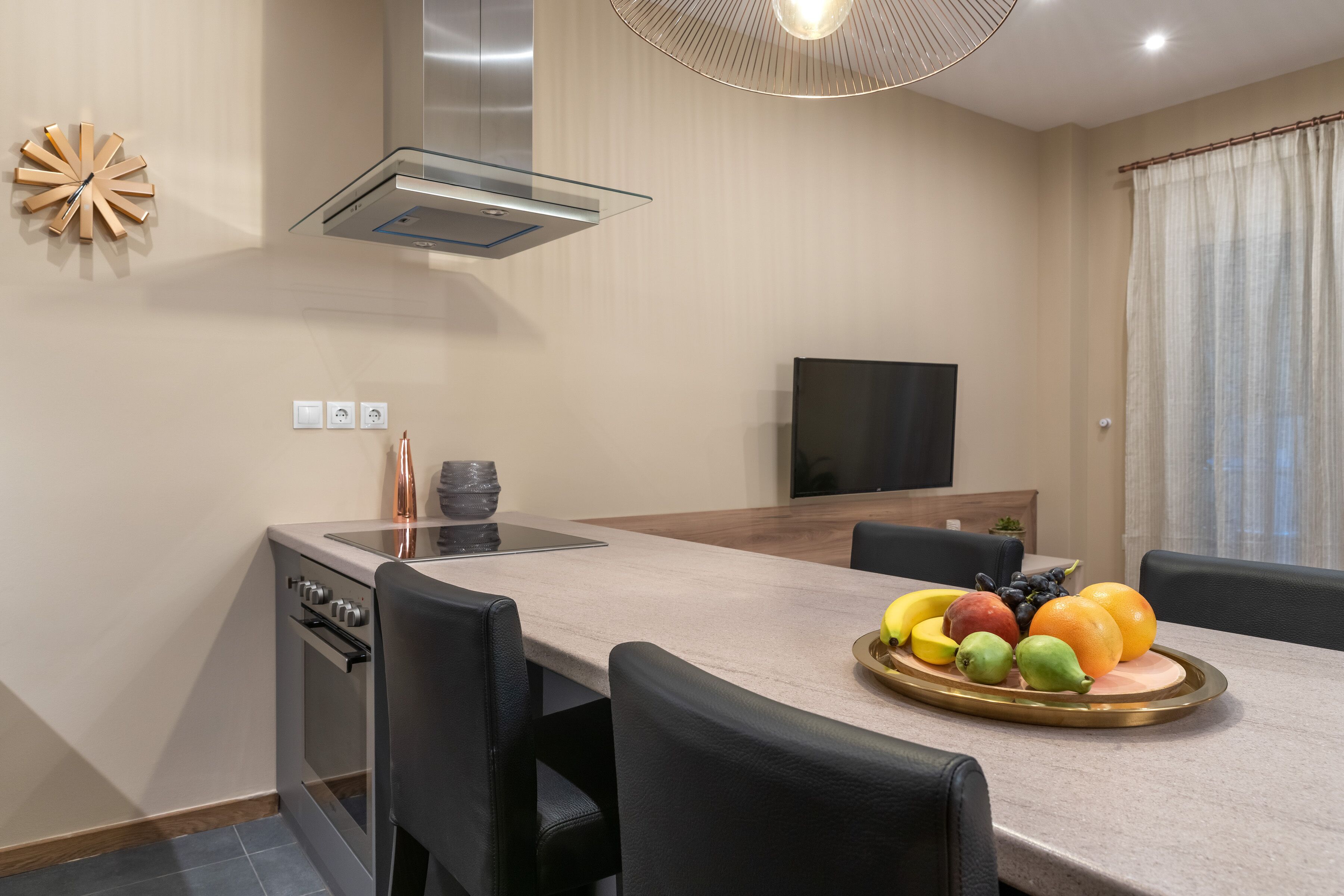 Una cocina moderna con horno empotrado, una mesa de comedor con sillas y una bandeja de fruta.