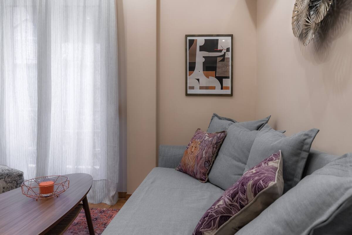 Un salon avec un canapé gris, une œuvre d’art abstraite encadrée et une décoration murale.