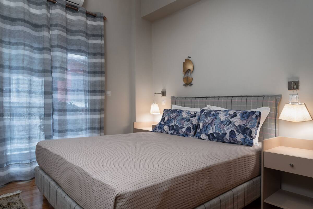 Une chambre à coucher bien rangée, avec un lit, deux tables de chevet, une lampe et un luminaire fixé au mur.