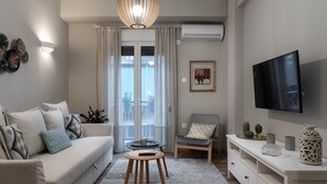 A living room with a sofa, a coffee table, a chair, a TV, and a decorative wall. - Absolute Athens Apartments (Athens)