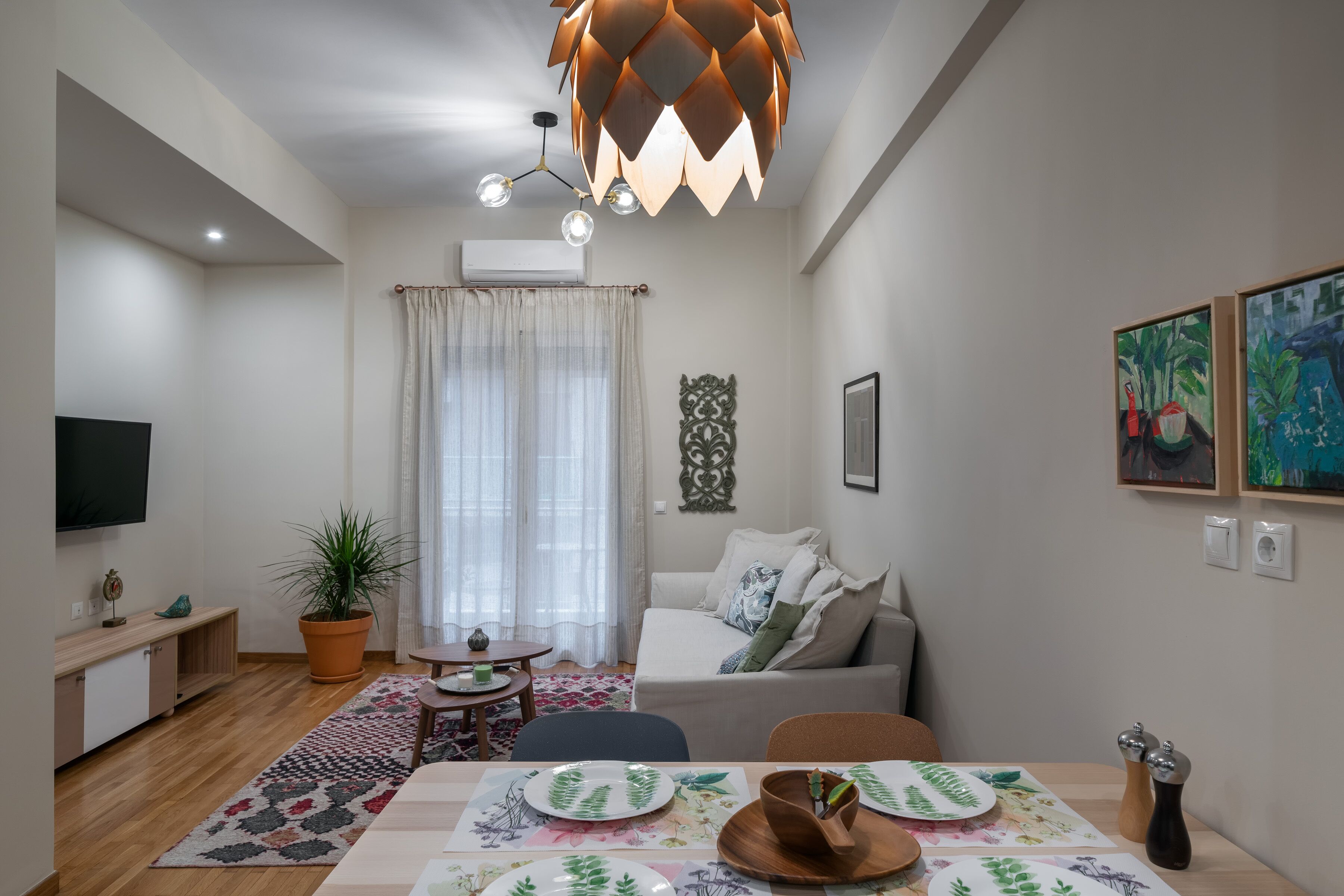 Una sala moderna con un sofá, una mesa de comedor con platos, un televisor y una lámpara de techo.