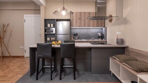 A modern kitchen with a central island, black bar stools, a hanging light fixture, and a built-in oven. - Absolute Athens Apartments (Athens)