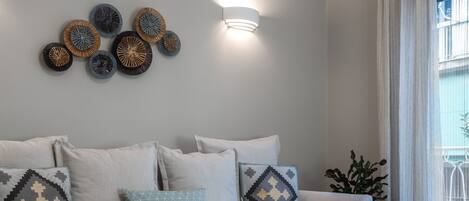 A modern living room with a grey sofa, patterned cushions, a small wooden table, and a decorative wall piece.