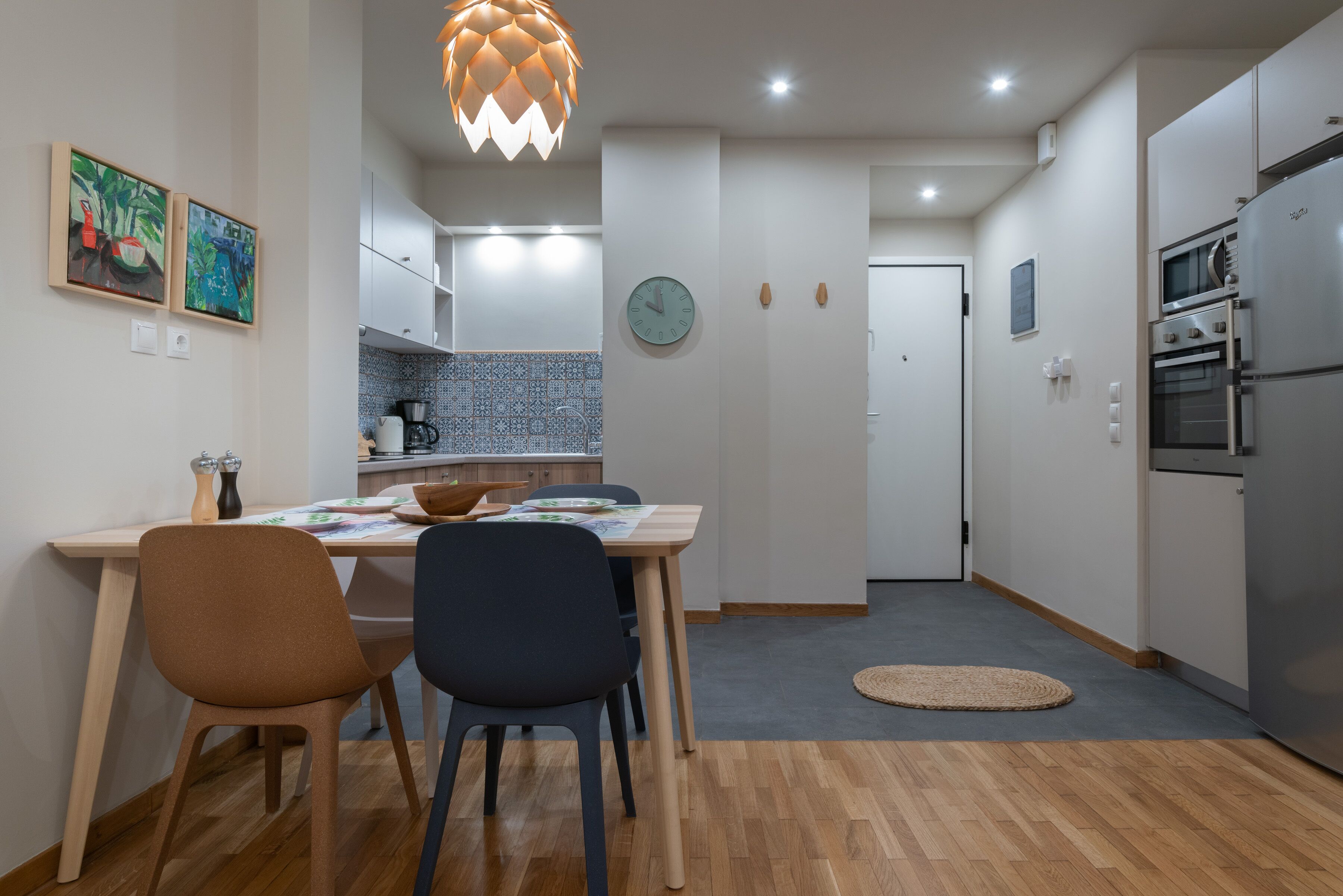 Una cocina moderna con piso de madera, una mesa de comedor con sillas, un reloj y un refrigerador.
