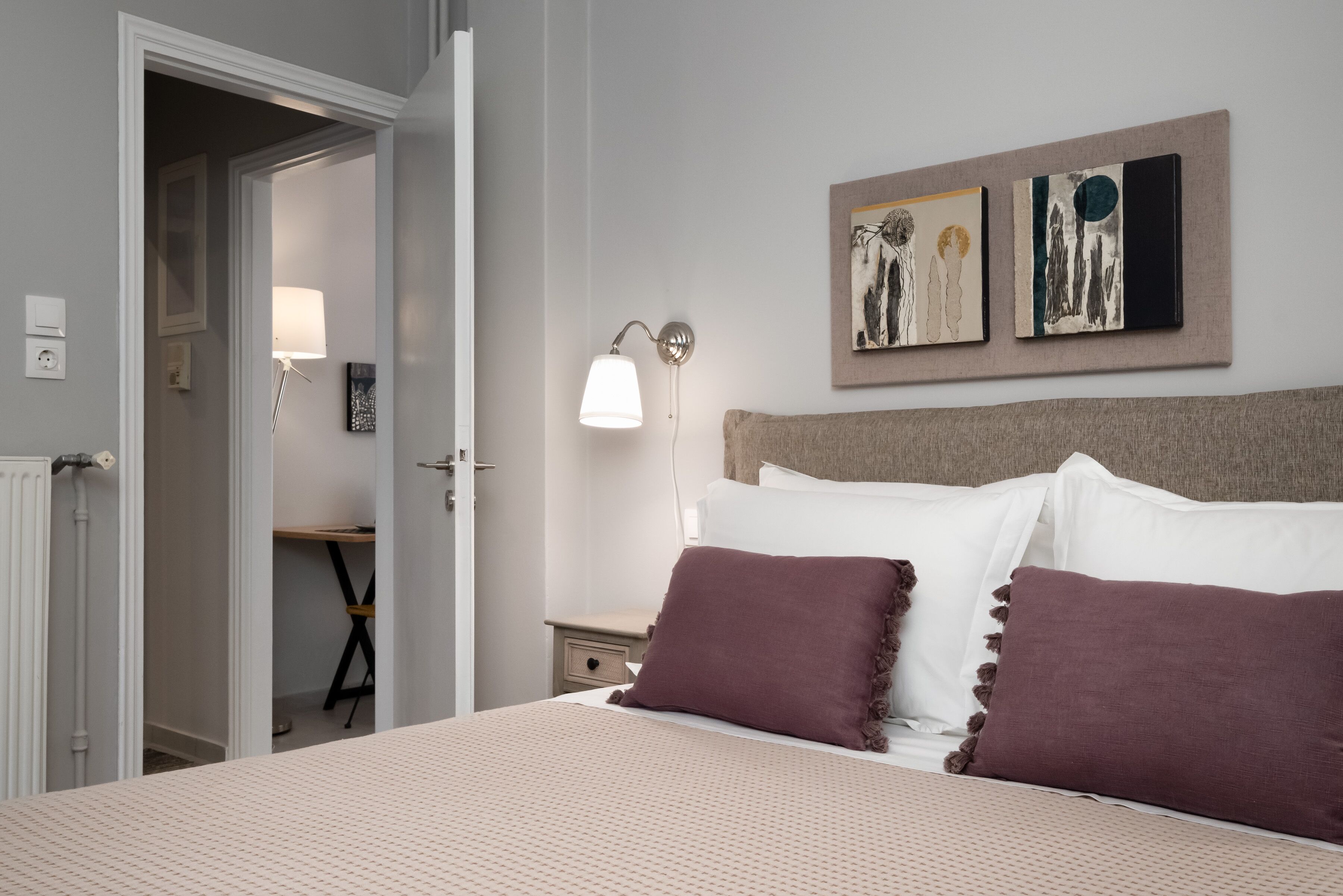 A neatly arranged bedroom with a bed, pillows, a bedside lamp, and artwork on the wall.