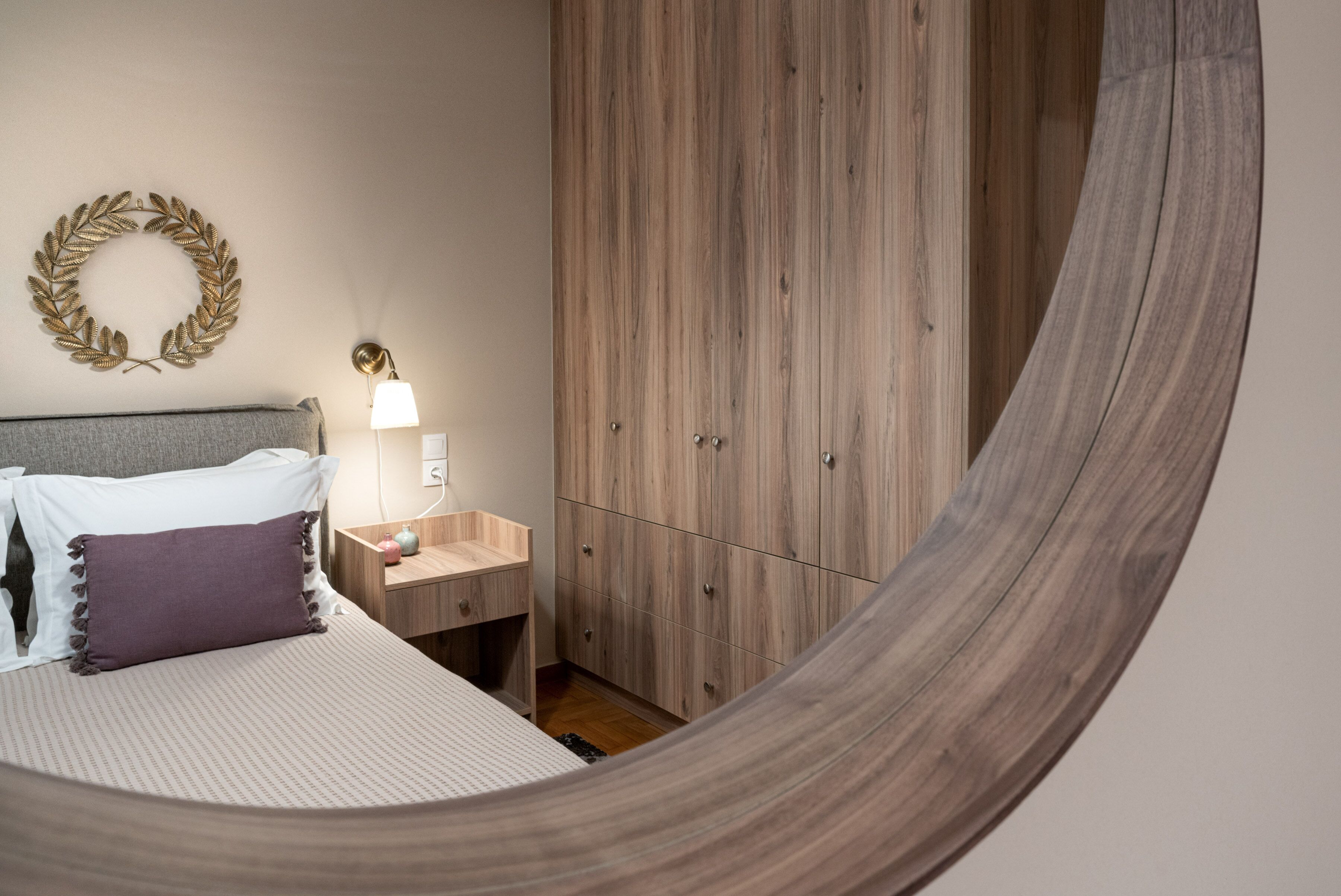 A bedroom with a bed, bedside table, lamp, wardrobe, and a wall-mounted wreath.