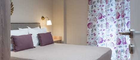 Quarto com cama, abajur, cortina florida e piso de madeira.