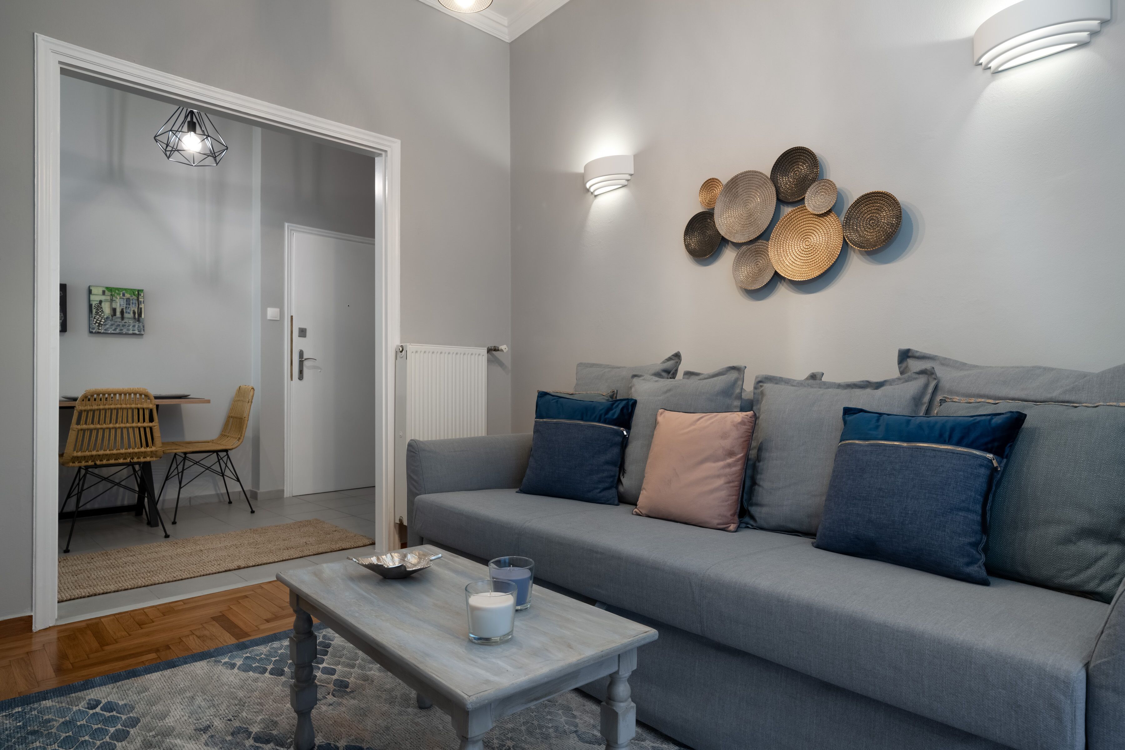 A modern living room with a grey sofa, a wooden coffee table, and a dining area with a wicker chair and table.