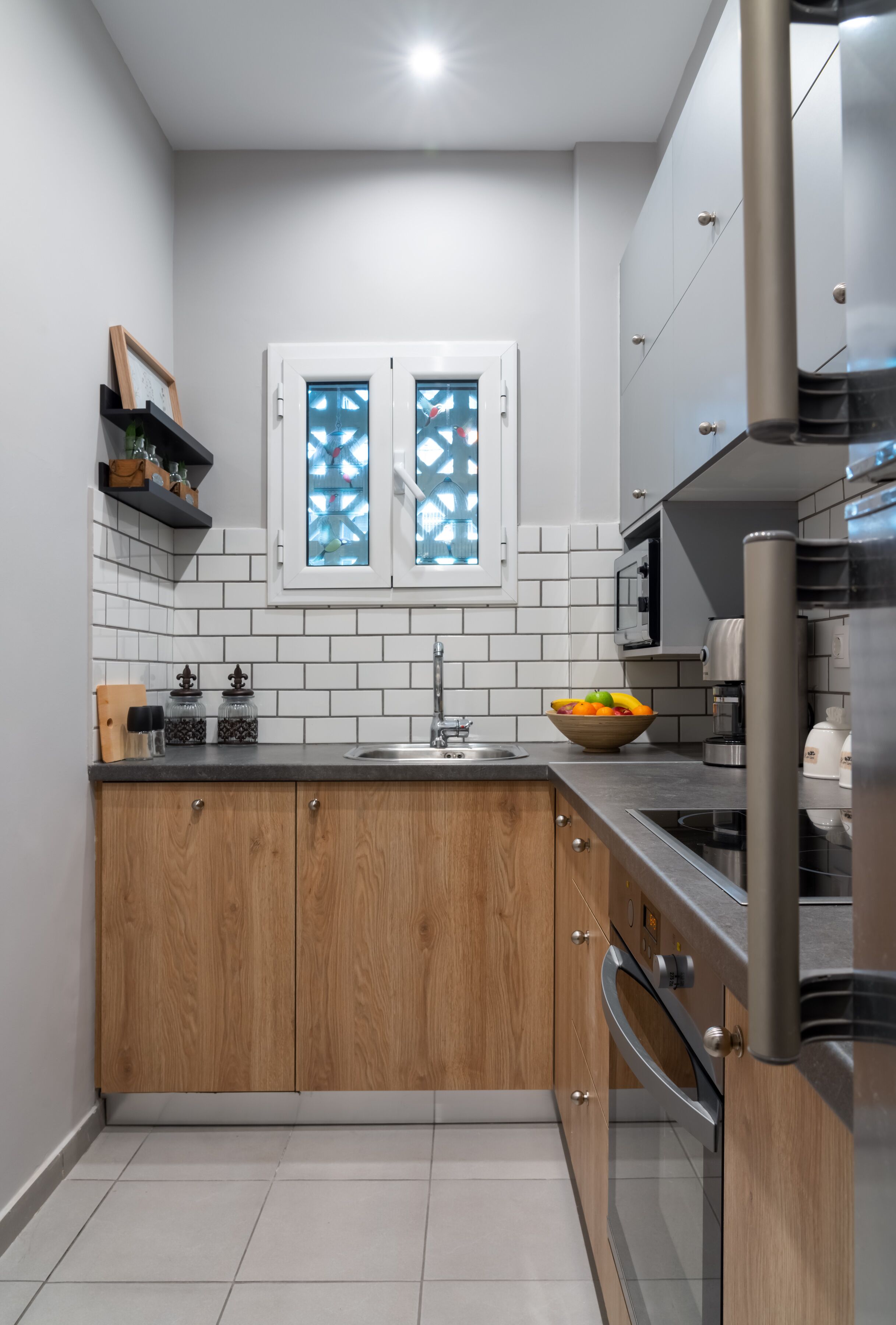 A modern kitchen with white subway tiles, wooden cabinets, a stainless steel refrigerator, and a window with decorative glass.