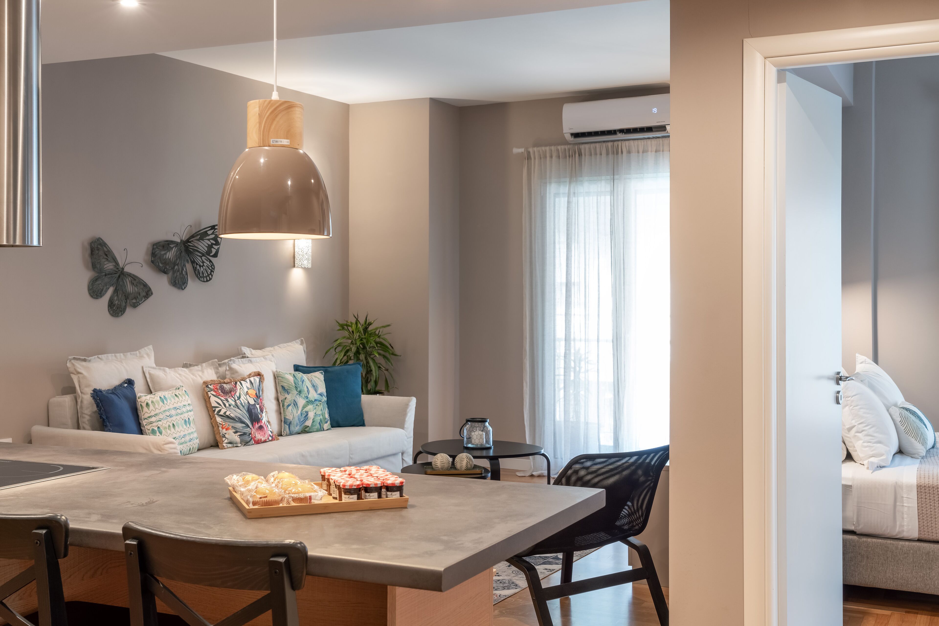 Un salon moderne avec un canapé, une table à manger et une table basse. On y trouve une plante, une lampe et une fenêtre avec des rideaux.