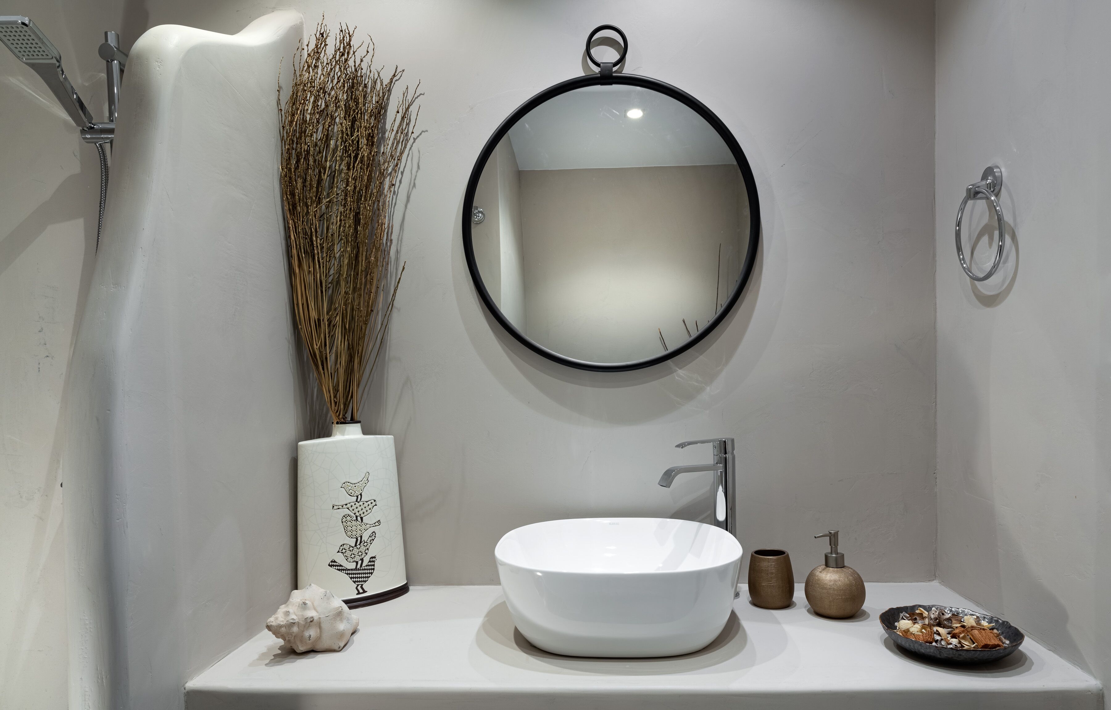 Un baño con un lavamanos blanco, un espejo redondo, una ducha y objetos decorativos.