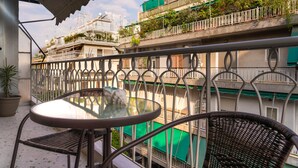 A balcony with a glass table and wicker chairs, overlooking a residential area with balconies and greenery. - Absolute Athens Apartments (Athens)