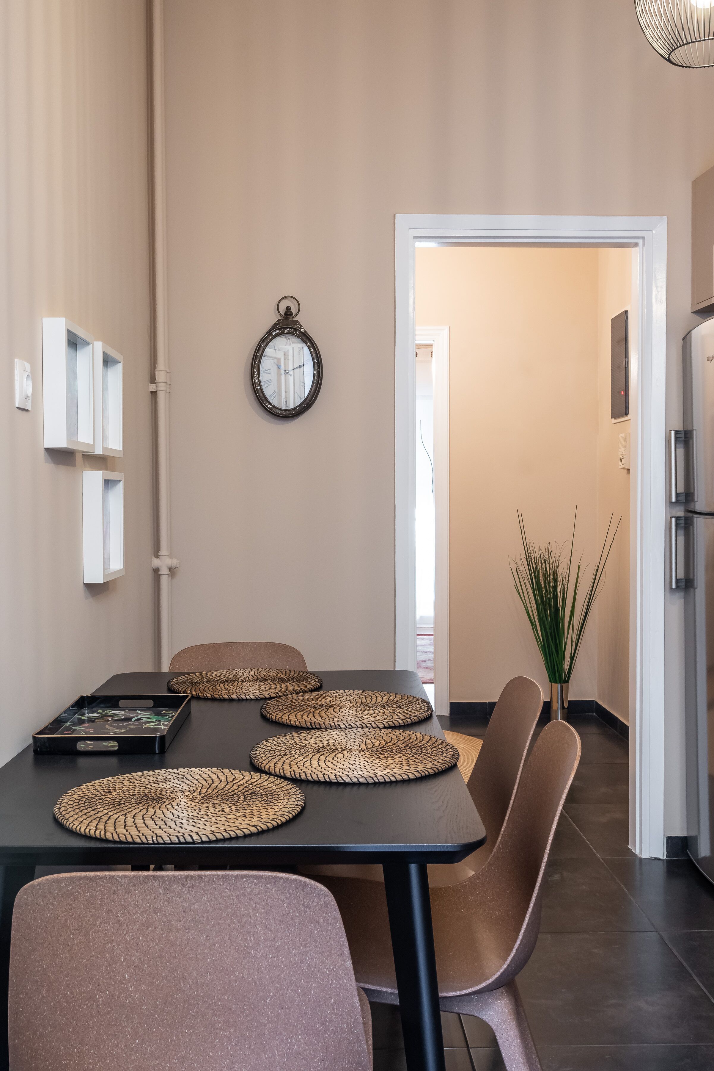 A dining area with a table set for four, a potted plant, and a modern kitchen in the background.