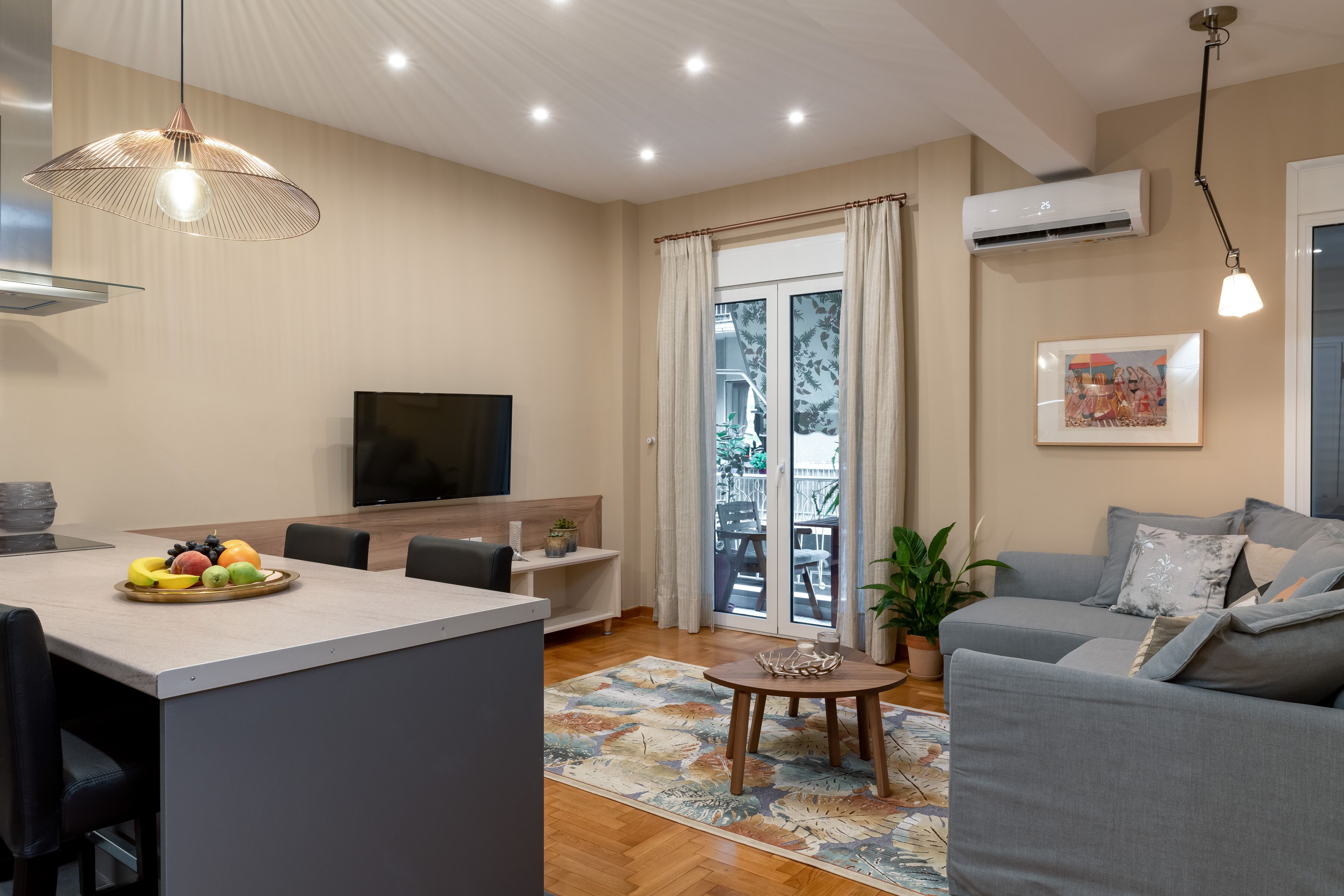 Una sala de estar moderna con un sofá gris, una televisi ón, una zona de comedor con fruta y un balcón con cortinas.
