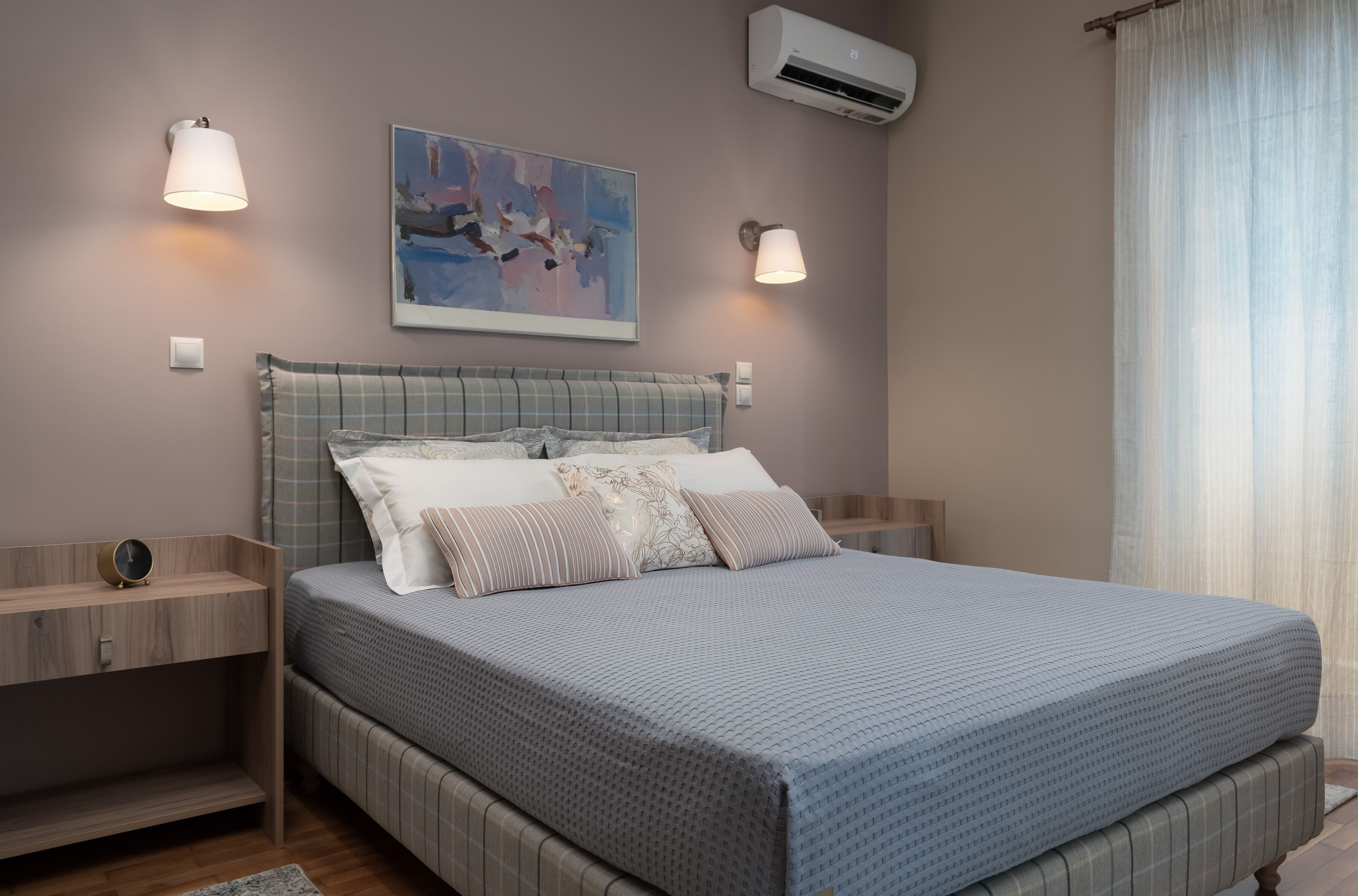 A bedroom with a bed, bedside tables, a wall-mounted air conditioner, and a painting.