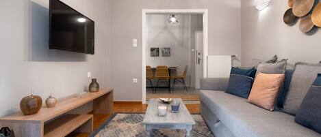 A modern living room with a flat-screen TV, a wooden bench, a coffee table, and a grey sofa with cushions.