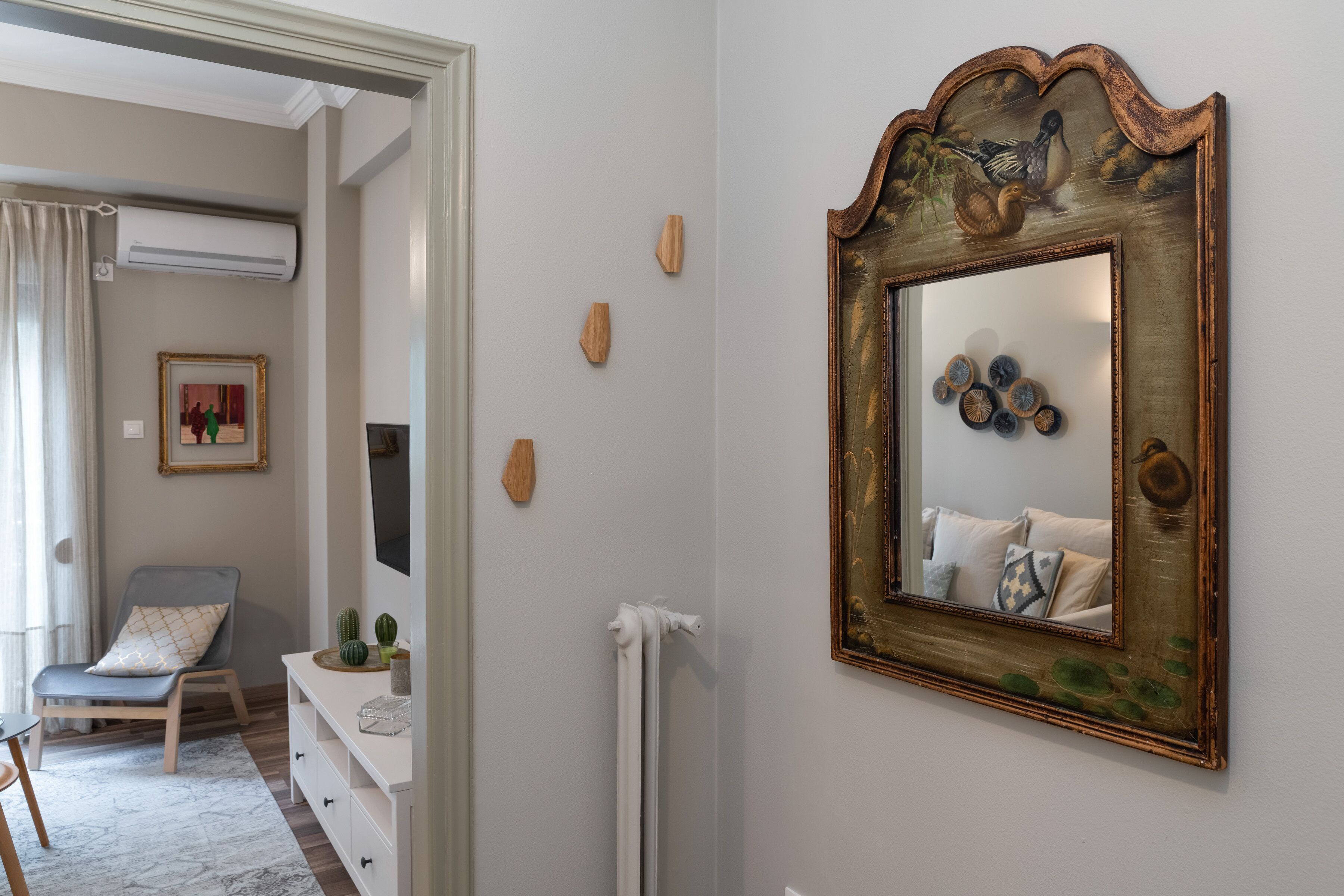 Une pièce comprenant une commode blanche, une chaise, un miroir avec un cadre décoratif et une petite table sur laquelle se trouve un cactus.