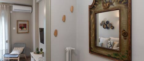 A room with a white dresser, a chair, a mirror with a decorative frame, and a small table with a cactus.