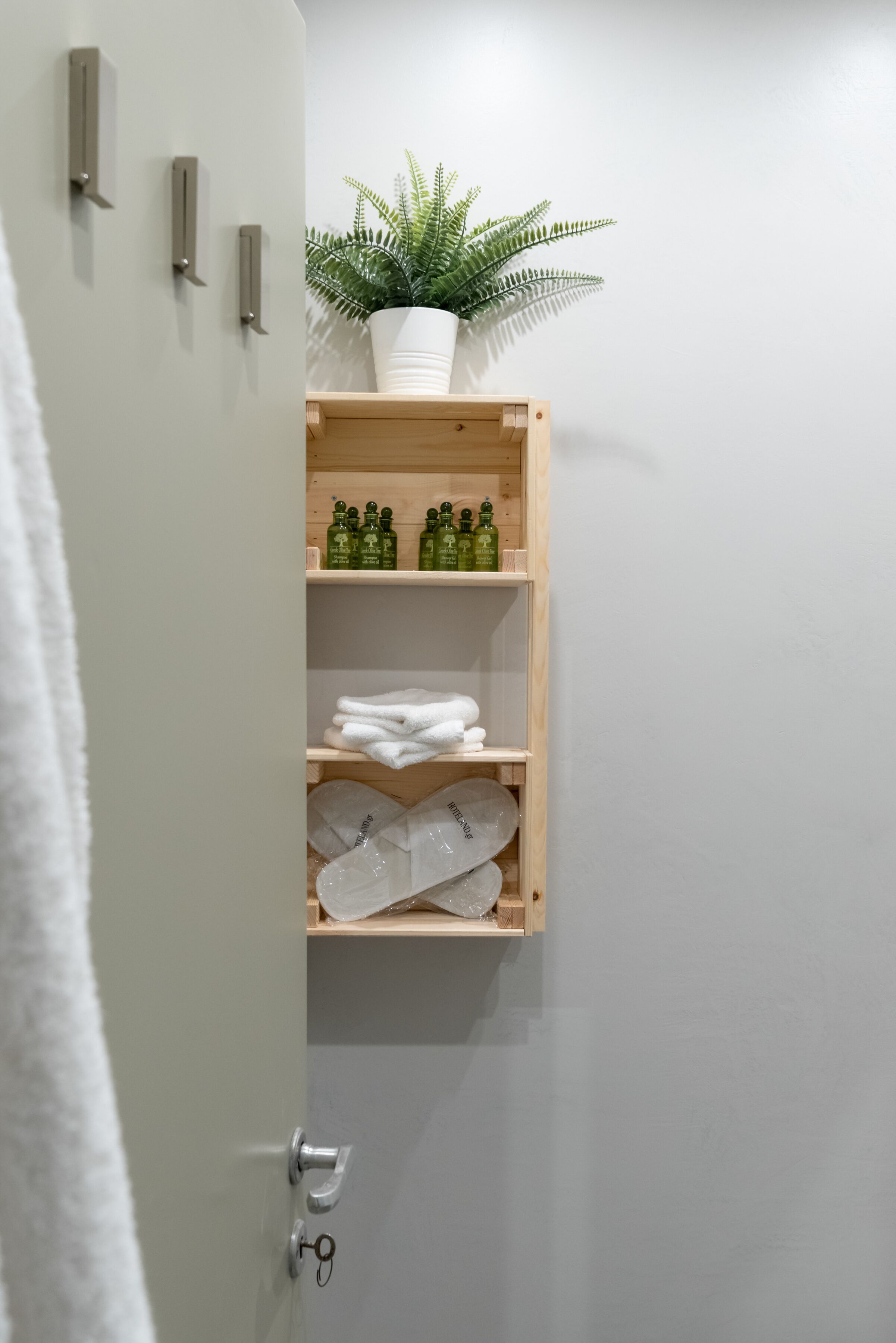 A bathroom with a wooden shelf holding toiletries, a potted plant, and neatly folded towels.