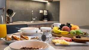 A breakfast table with various food items, a coffee maker, and a glass of orange juice. - Absolute Athens Apartments (Athens)