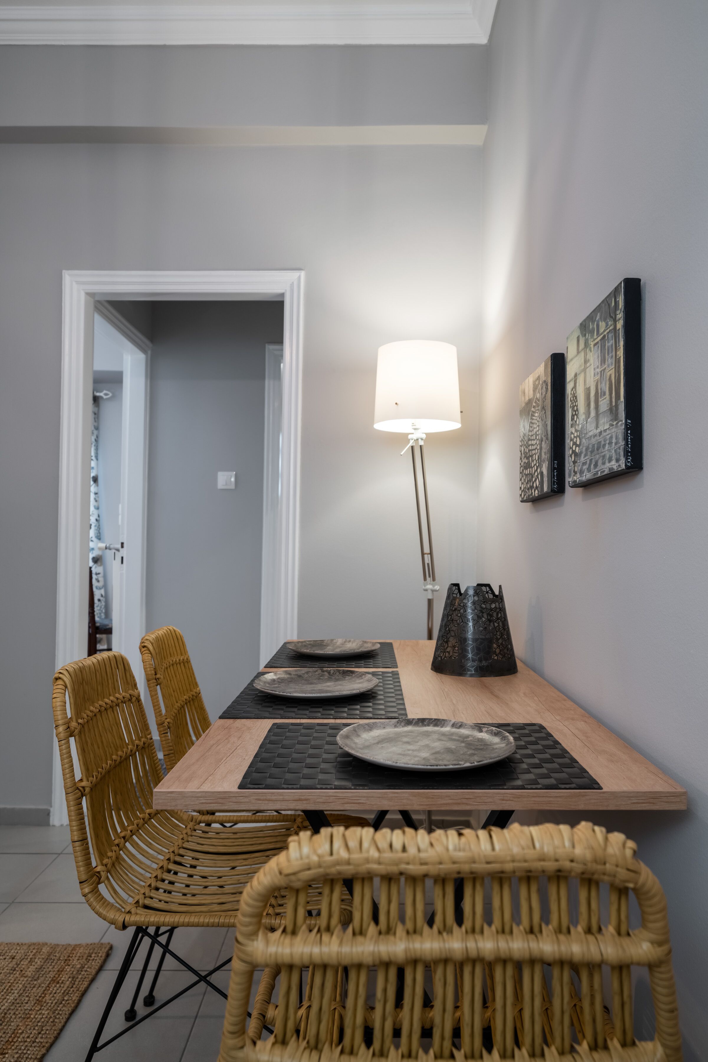 Un coin repas avec une table en bois, des chaises en osier, un lampadaire et des œuvres d’art accrochées au mur.