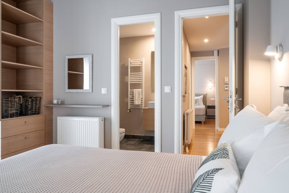 Une chambre à coucher avec un lit, une armoire, un radiateur et une salle de bain visible à travers une porte ouverte.