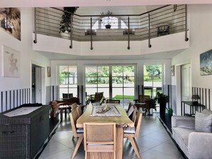 A spacious dining area with a high ceiling, large windows, and a view of the outdoors.