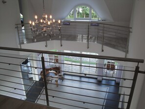 A spacious interior with a high ceiling, a chandelier, a staircase, and a view of the outdoors through a large window.