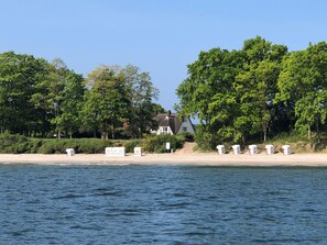 A coastal house with a beach view, surrounded by trees and a calm sea.