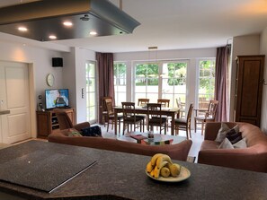 A modern living room with a dining area, a television, and a fruit bowl on the coffee table.