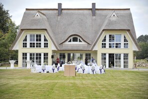 A building with a thatched roof, large windows, and a lawn with white chairs.